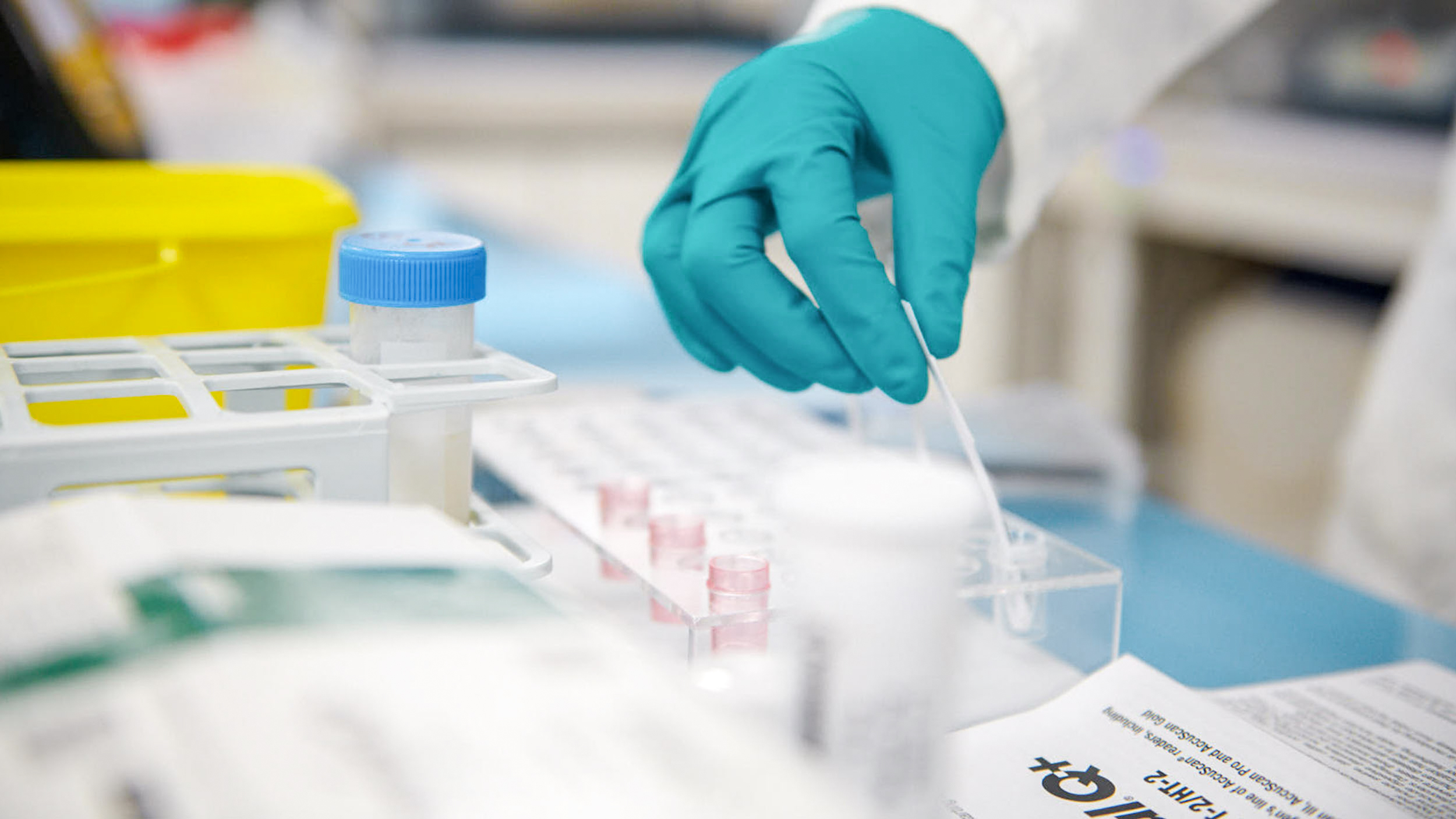 A lab worker wearing blue latex gloves carrying out tests