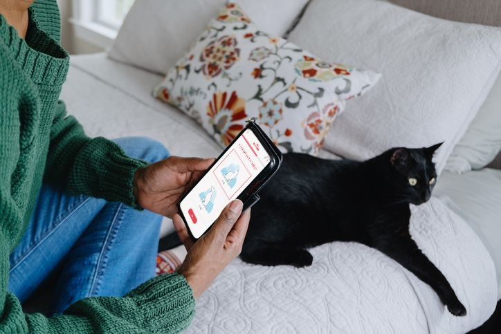 woman checking her phone while sitting on bed with a cat