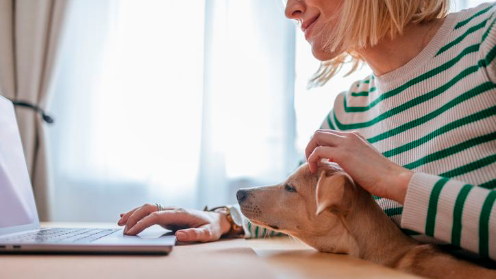 Vrouw checkt Royal Canin Voedingswijzer op haar laptop terwijl ze haar puppy op schoot aait