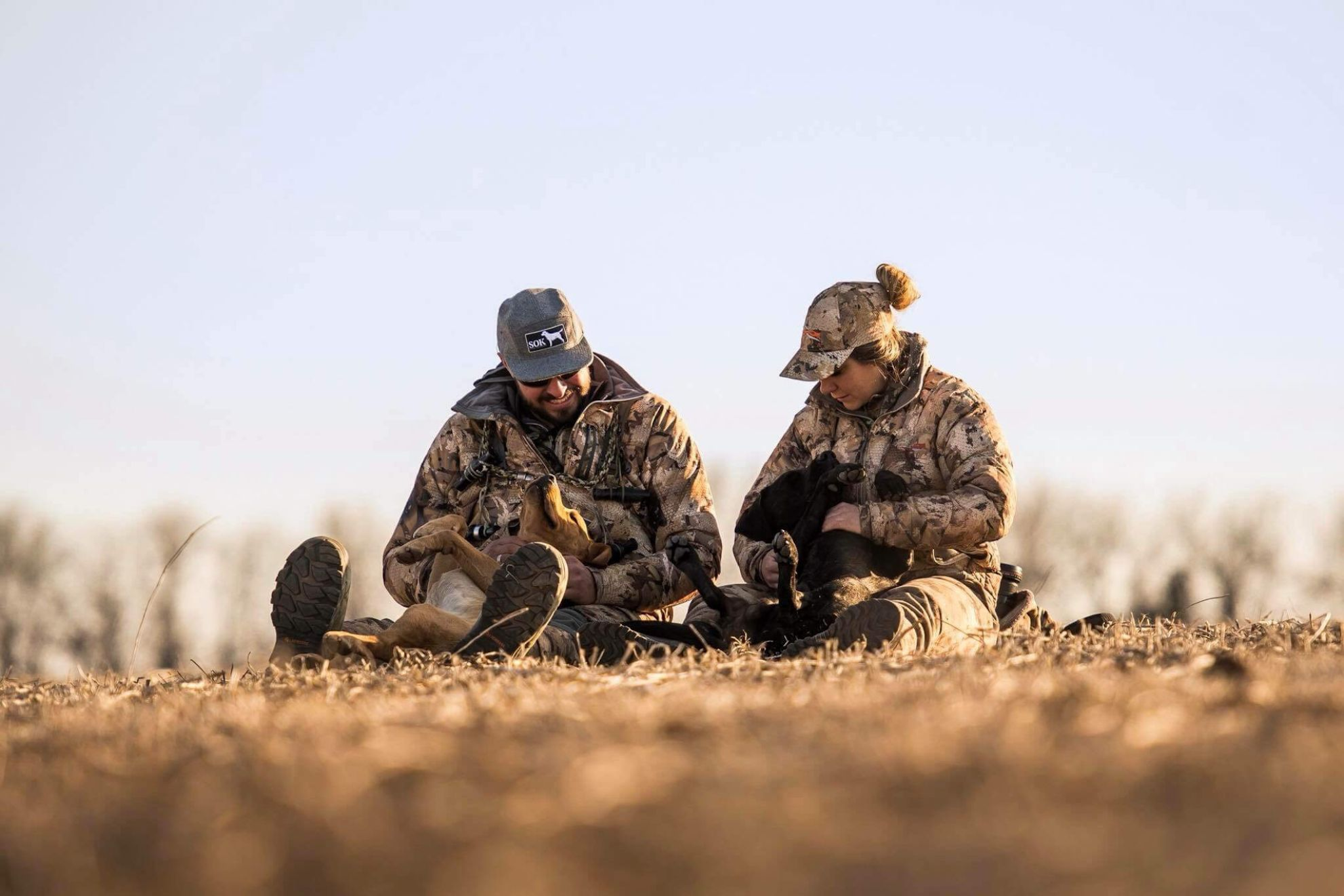 Man and woman taking a break with their Labs during a waterfowl hunt